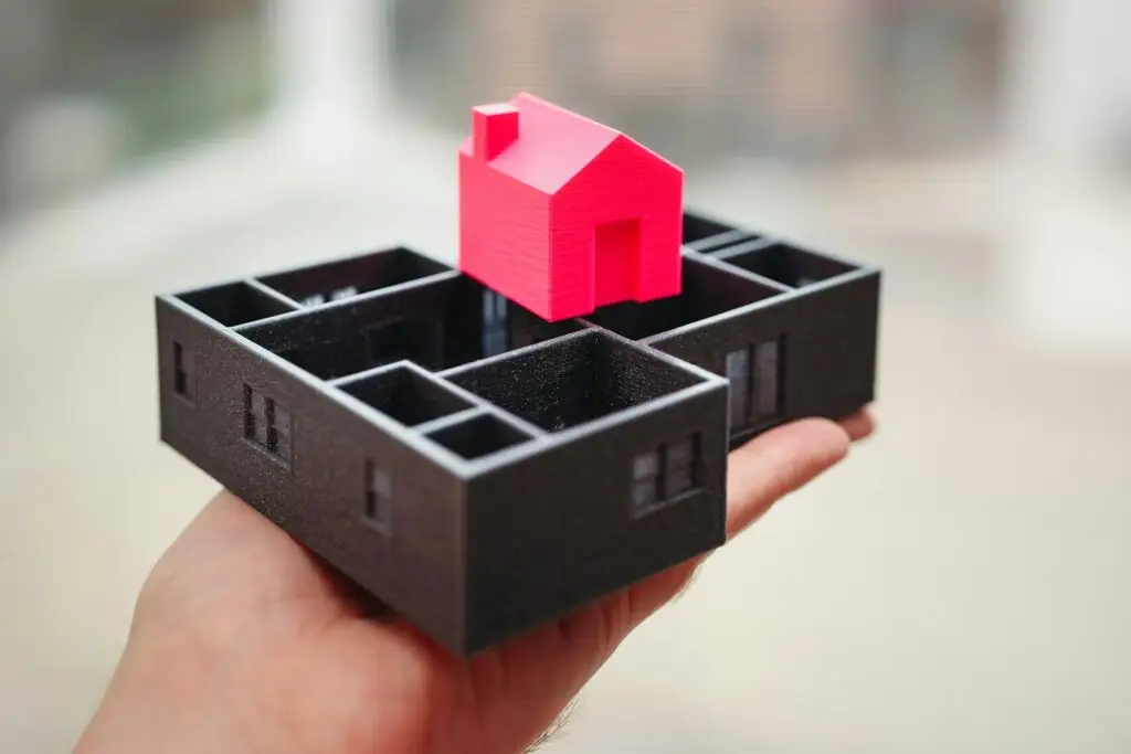 A hand holding a black box with a red house in it